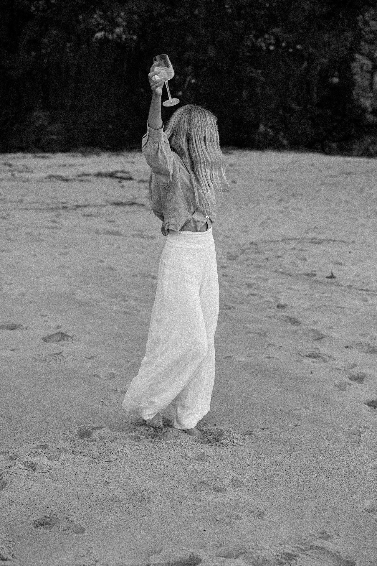 Woman raising champagne glass on the beach at dusk